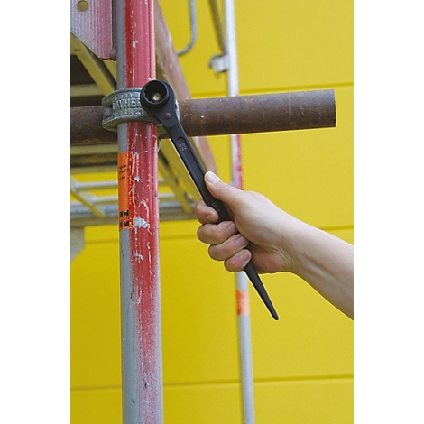 Eine Hand hält einen schwarzen Schraubenschlüssel an einer roten Gerüststange.